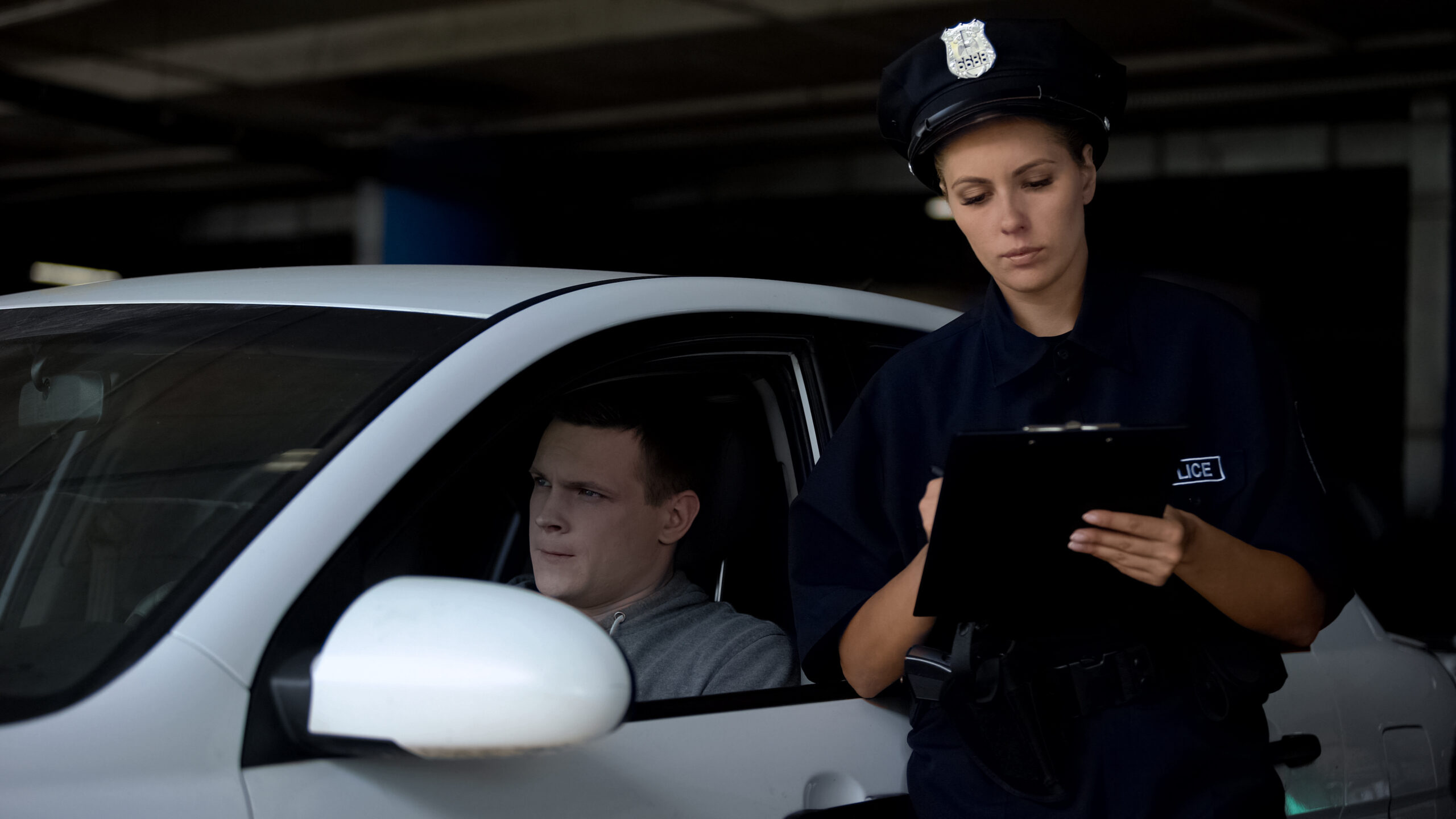 Female officer writing traffic ticket to male driver for parking violation.