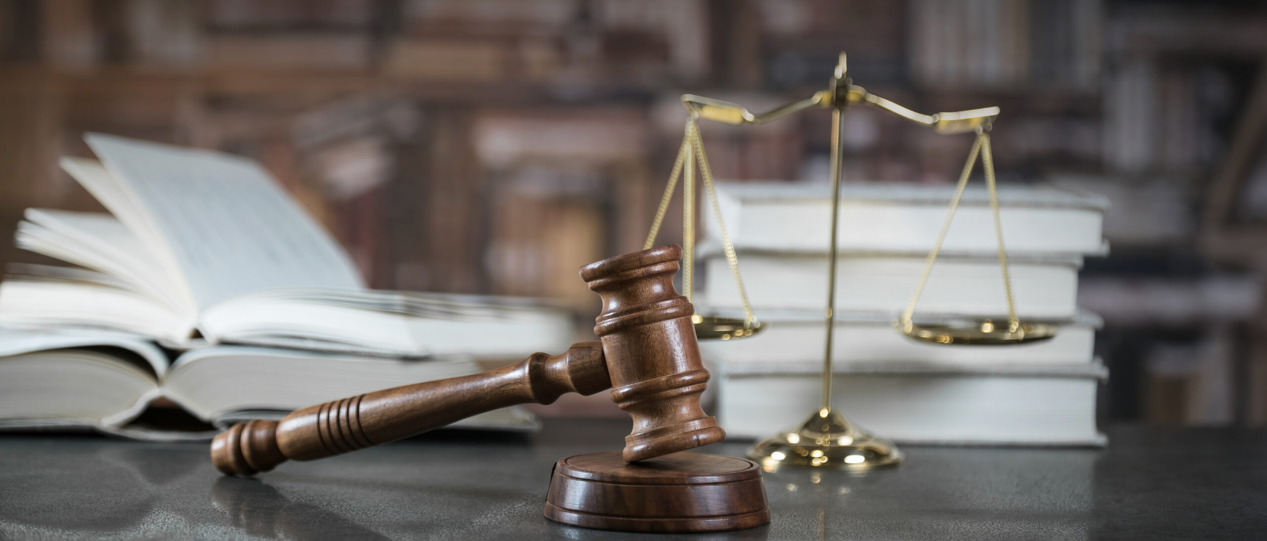 Scales of justice, a wooden gavel, and books are on top of a lawyer's desk.