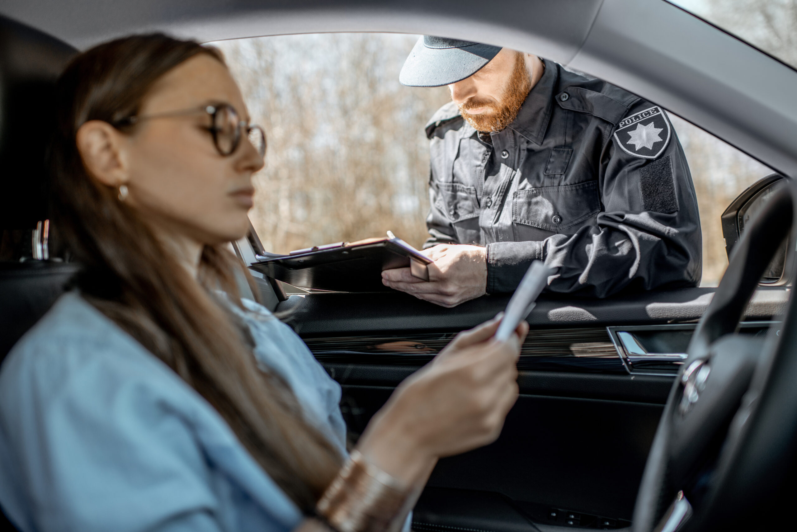 Policeman checking documents of a young female driver sitting in the car, view from the car interior.