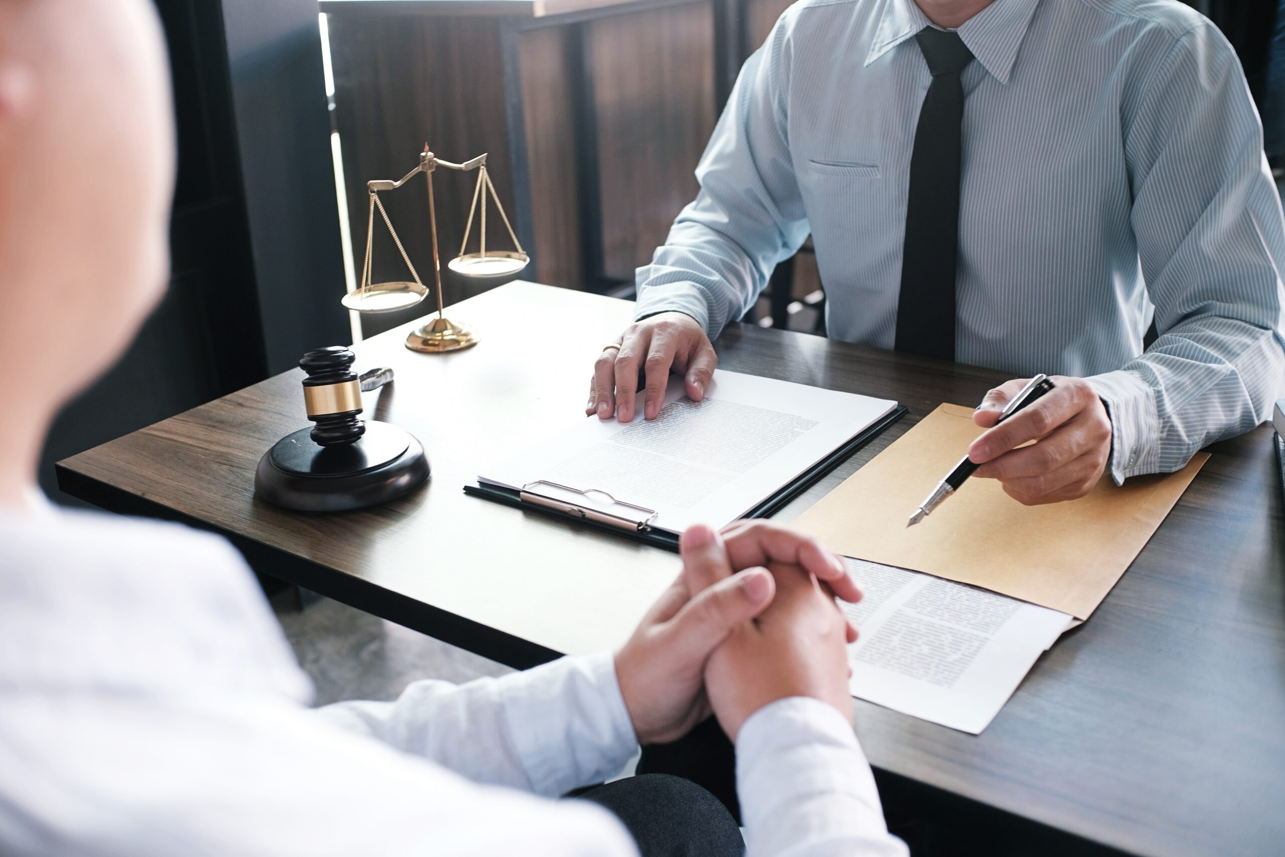 Legal counsel presents to the client a signed contract. a gavel and scales of justice is on top of the wooden table.